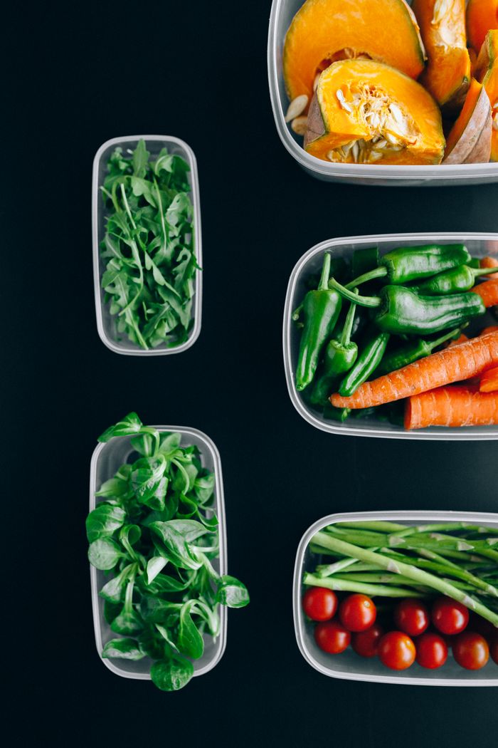 Vibrant assortment of fresh vegetables in plastic containers on a black background, showcasing healthy eating.
