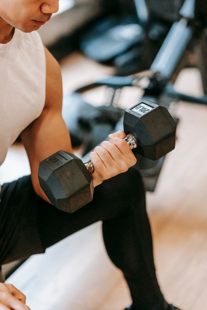 Side view of crop male athlete lifting dumbbells while doing bicep curls in modern gym